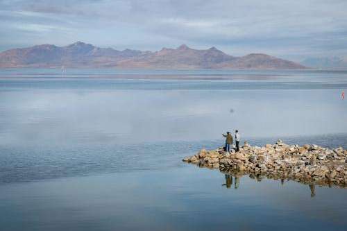 Visitors on Silver Sands Beach at Great Salt Lake State Park, near Magna, stand on rocks jutting out into the iconic saline lake with Antelope Island seen in the background, Jan. 27, 2024. Jim Hill, KUER